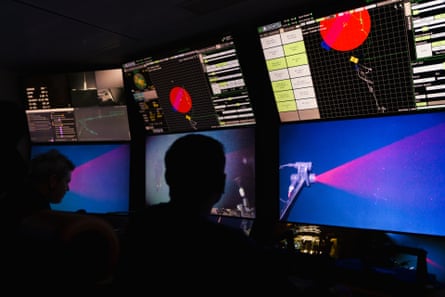 Silhouette of two people sat in front of multiple screens showing underwater images
