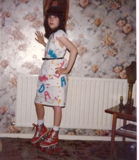 Tracy King in 1989, aged 13, standing in roller skates leaning against a living room wall with floral wallpaper