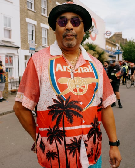 A man wearing a Hawaiian shirt with an Arsenal logo, sunglasses and a hat.