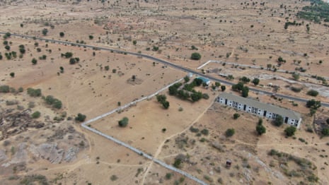 Aerial photograph of a building by a road amid a bare desert landscape dotted with trees and shrubs