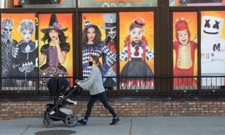 A woman pushing a pram past a colourful shop window displaying Halloween items