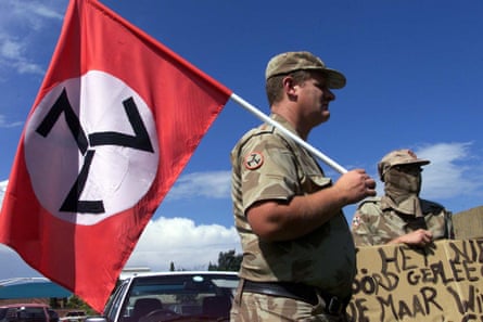 A man in military fatigues holds a swastika-like flag.