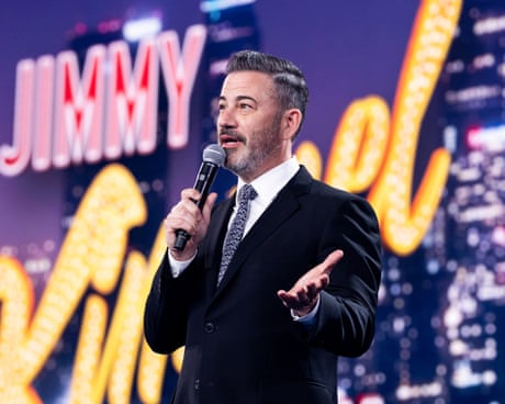 a man in a suit speaks in front of a backdrop that reads Jimmy Kimmel