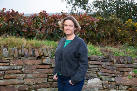 Sam Kirby in a cardigan next to a drystone wall in her garden