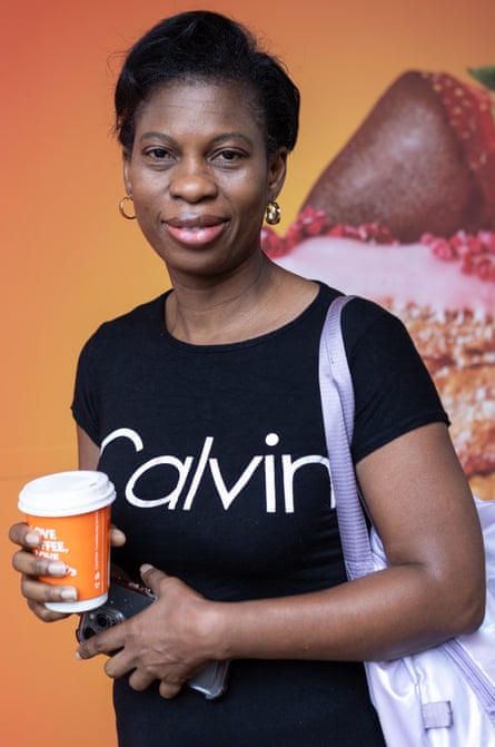 Vida Amos, with a shoulder bag, hoop earrings and a T-shirt labelled "Calvin", holds a coffee cup in one hand and her phone in the other, slightly smiling