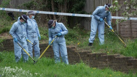 Forensic officers search a path between banks of grass.
