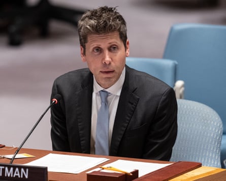 Sam Altman sits at a desk behind a microphone