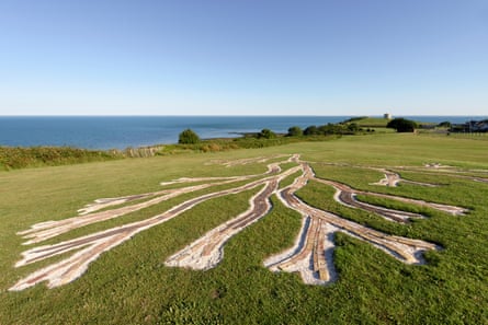 A seaweed-shaped sculpture of bricks set in the grass by a cliff, with the sea in the background