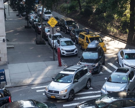 Rush hour traffic in New York City along moves along a street lined with parked cars