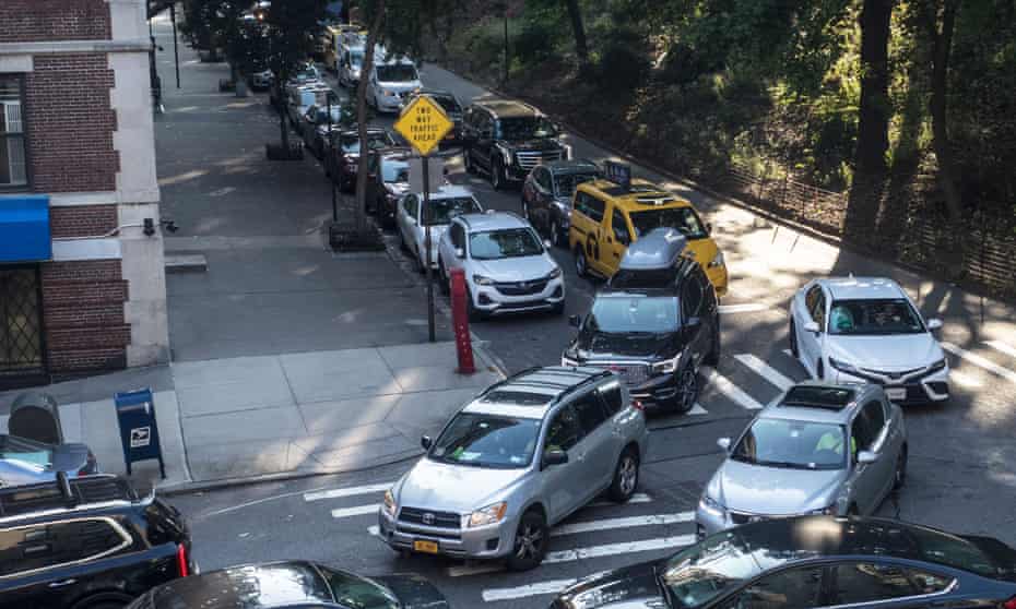 Rush hour traffic in New York City along moves along a street lined with parked cars