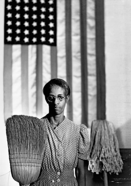 A woman holding a broom and a mop in front of an American flag.