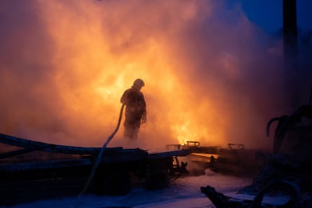 A figure holding a hose is silhouetted by flames