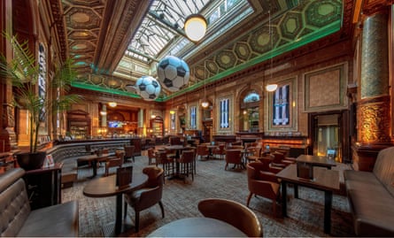 An internal view of a large elaborate Victorian pub room with tiling, skylight banquettes and club chairs