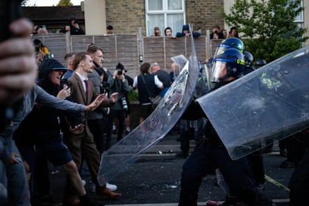 Riot police push forward with shields during unrest in Southampton. Jahn can be seen in a suit and tie at the front of the line of protesters
