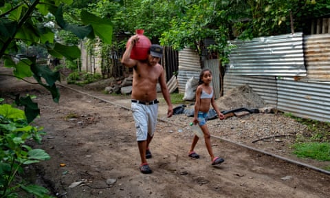 Victor Funez and his daughter Patricia carry water pitchers back to their house after filling them up at a cemetery tap.