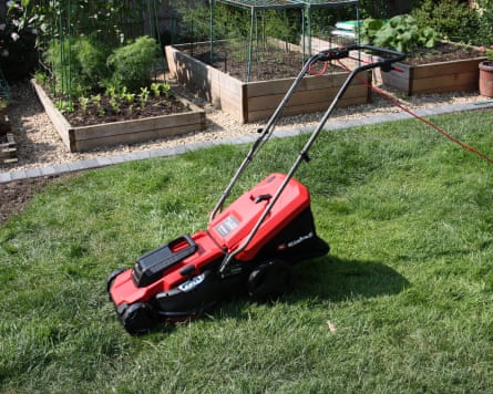 A red and black Einhell lawnmower on the grass of a garden