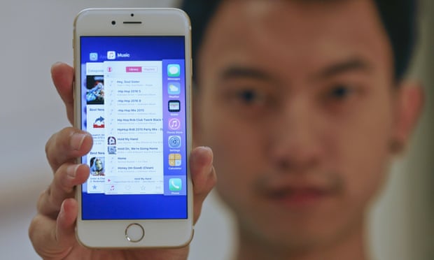 A sales assistant shows features of iOS9 on an Apple iPhone 6, which comes with the option of installing an ad blocker.