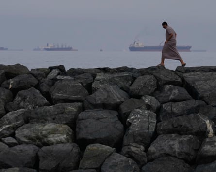 FILE- A man walks along the shore as oil tankers and ships line up in the Strait of Hormuz, seen from Khor Fakkan, United Arab Emirates. Iran is accused of using the strait as leverage.