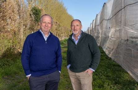 Two men stand in a field that contains a large mesh covering