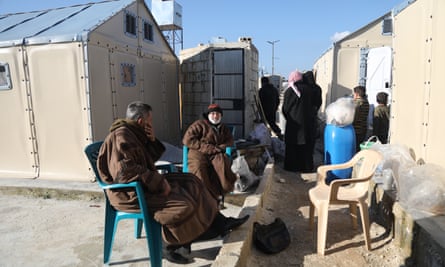 People rest in front of flat-pack shelters.