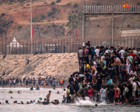 People crowd on to a fence that extends into the sea