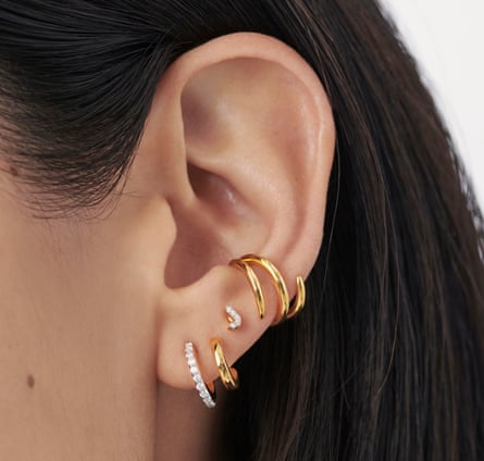 A model’s ear showing her earrings, which are one gold and diamond hoop, a small gold hoop, a diamond stud in the shape of the letter J and a gold ear cuff