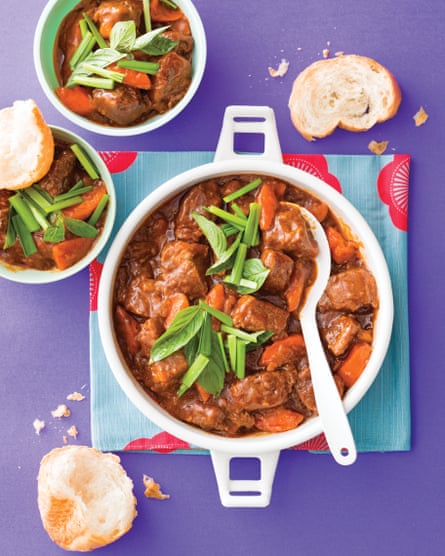 Tampilan atas semangkuk sajian putih bulat berisi sup daging sapi yang dimasak lambat dengan wortel, dan hiasan kemangi Thailand dan kucai bawang putih, di permukaan ungu