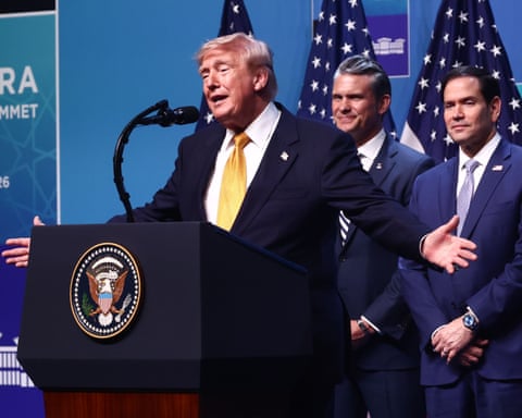 President Trump speaks at a podium with the presidential seal, flanked by two men in suits