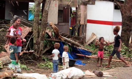 A woman carrying a baby stands with children outside homes damaged by Cyclone Pam in Port Vila.