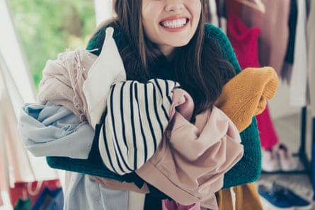 Une femme souriante tenant un paquet de vêtements dans ses bras.