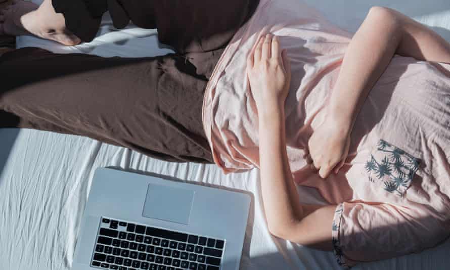Young person lies on bed next to laptop, face not visible