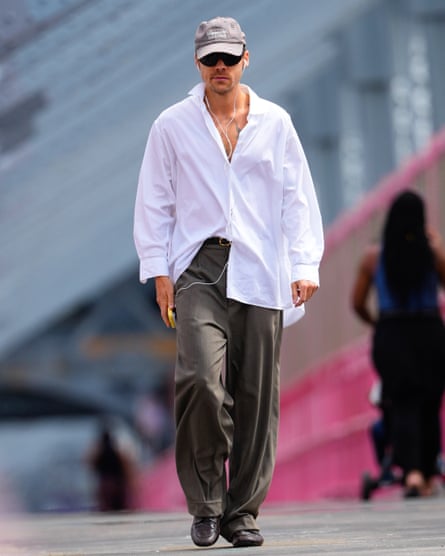 Harry Styles strolling in baggy trousers, oversized white shirt, sunglasses, baseball cap and loafers