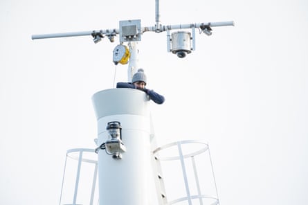 A woman seen in a tubular viewing platform at the top of a ship’s mast