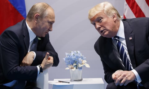 Vladimir Putin leans over in his chair to speak to Donald Trump, his thumb pointing past the camera.