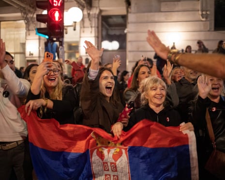 In Belgrade, a cheering crowd raises hands, holding a Serbian flag at night