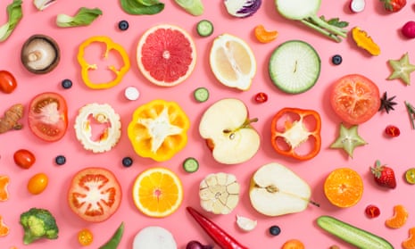 Colourful flat lay view of different types of sliced fruits and vegetables on a pink background.