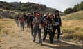 Migrants hold hands as they stride towards a gap in the border wall