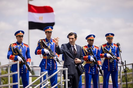 A man in suit flanked by men in smart military uniforms holding guns with an Egyptian flag behind them