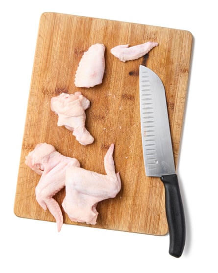 Chicken wings cut into pieces on a wooden board with a sharp knife
