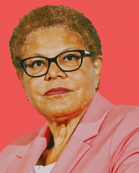 Image of Karen Bass, in pink blazer, with pink background, looking serious.