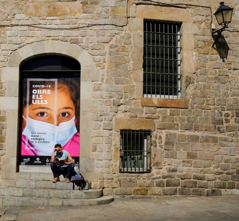 A man reading a book next to a poster that says “Covid-19, open your Eyes”, in Barcelon, Spain.