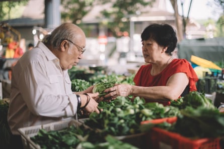 A woman vegetable seller talking to a male customer who is inspecting a small head of lettuce.