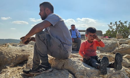 A boy, adult man and elderly man sit on stony ground