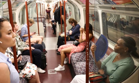 A woman uses a hand held fan to cool down while travelling on the London underground during hot weather.