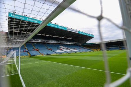 View through the net of a goal of green grass pitch and spectator stands at Elland Road.