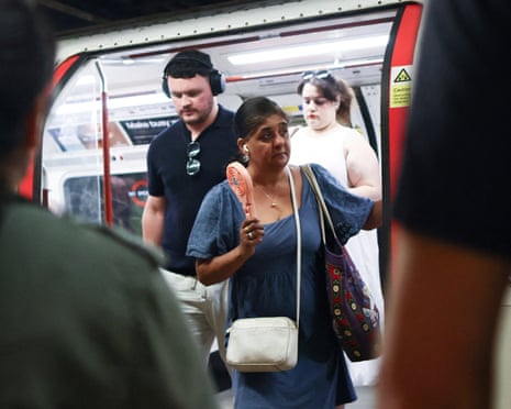 A woman uses a fan on the tube, with other passengers in the foreground