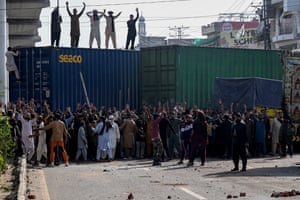 Protesters stand on shipping containers, which block a road