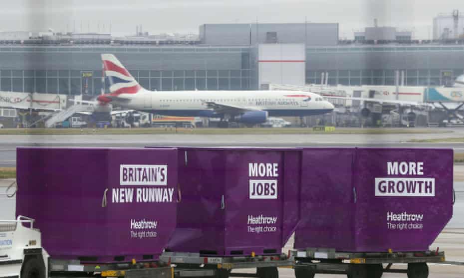 A British Airways plane taxis behind cargo containers adorned with ‘Britain’s New Runway’ at Heathrow.