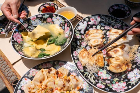 A table setting featuring a bowl of soup dumplings, a plate of frie dumplings, and a plate of boiled dumplings with a spicy dressing.