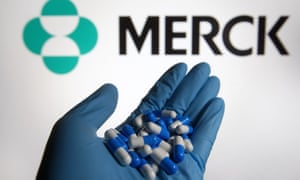 In this photo illustration, medicine pills in form of capsules are seen in a hand dressed in a medical glove, with a Merck & Co., Inc. logo of a pharmaceutical company in the background.